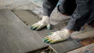 tiler is installing ceramic floor tiles above cement and electric floor heating, aligning, using building level, modern technology of repair, close up shot